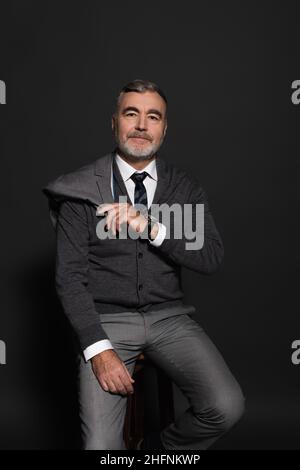 Positiver Geschäftsmann mit Blazer, während er auf der grauen Kamera sitzt Stockfoto