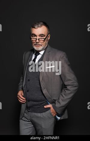 Ein Geschäftsmann im Anzug, der mit der Hand in der Tasche auf dunkelgrau steht Stockfoto