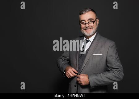 Erfolgreicher Geschäftsmann knöpfte Blazer, während er die Kamera auf Dunkelgrau ansah Stockfoto