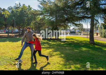 Aktiver Vater, der mit seiner Tochter im Teenageralter auf dem Rasen in einem schönen Park Fußball spielt. Sie haben eine gute Zeit mit der Familie, während sie trainieren. Spiel Stockfoto
