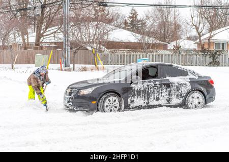 Ein Mann schaufelt Schnee vor dem Chevrolet-Fahrzeug, das an der Kreuzung von Victoria Park Avenue und York Mills feststeckt. Es ist ein Tag mit starkem Schneefall Stockfoto