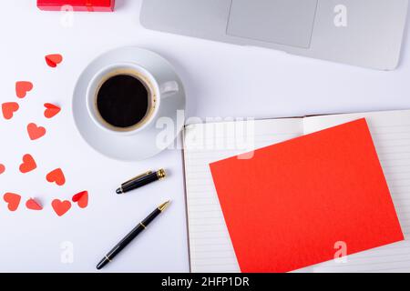 Leeres rotes Papier auf offenem Tagebuch mit Platz für Kopien bei Kaffee und Herzform am Schreibtisch Stockfoto