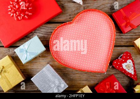 Deckenansicht einer leeren roten herzförmigen Geschenkbox mit Platz zum Kopieren inmitten von Geschenken auf einem Holztisch Stockfoto