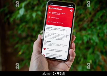 Eine Hand hält ein Smartphone mit einer Infektionswarnung im Corona-App Display Stockfoto