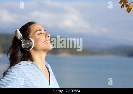 Glückliche Frau, die in einem See mit kabellosen Kopfhörern meditiert Stockfoto