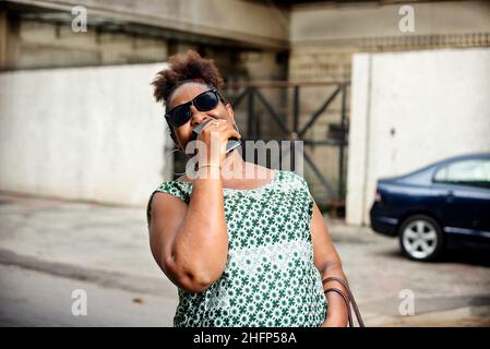 Schöne glückliche, reife Geschäftsfrau, die eine Sonnenbrille trägt und auf der Straße lächelt. Stockfoto