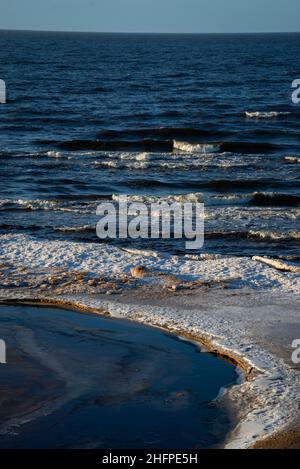 Eisiger Winterstrand am Meer mit gefrorenem Sand und Eisblöcken im Wasser. Kalte Dünen Stockfoto