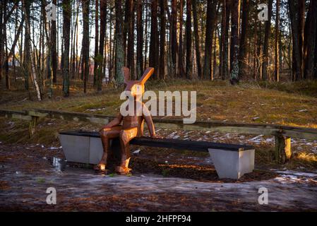 Ein hölzerner Osterhase, der auf einer Bank auf einem Touristenpfad sitzt. Stockfoto