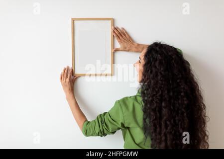 Weibliche Hängende Leere Bild In Rahmen An Weißen Wand Innen Stockfoto