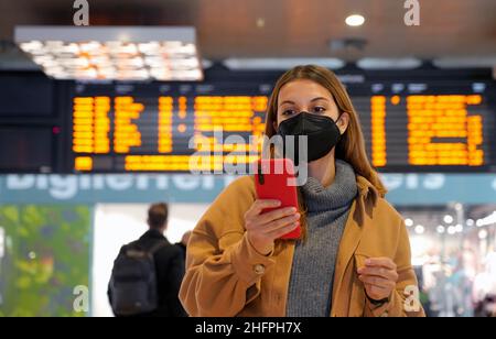 Reisende Frau trägt KN95 FFP2 Gesichtsmaske an der U-Bahn Station. Junge Frau mit hinter den Fahrplänen der Abflüge Ankünfte Informationen auf h überprüfen Stockfoto