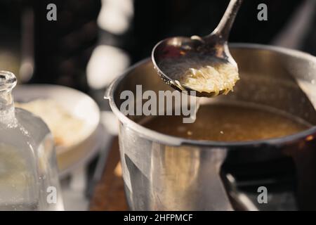 Nicht erkennbare Person, die Hühnernudelsuppe mit einer Pfanne aus einem Topf serviert. Nahaufnahme und selektiver Fokus Stockfoto