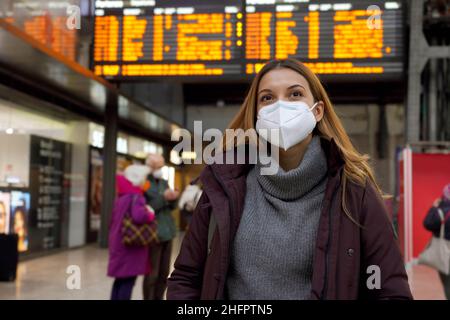 Reisende Frau trägt medizinische Gesichtsmaske am Flughafen. Glückliche junge Frau, die hinter den Fahrplänen der Abflüge nach oben schaut, geht b Stockfoto