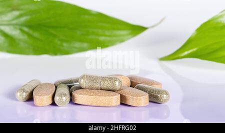 Kräutertabletten und Kapseln sowie grüne Blätter auf hellblauem Hintergrund aus nächster Nähe. Konzept der Kräutermedizin Stockfoto