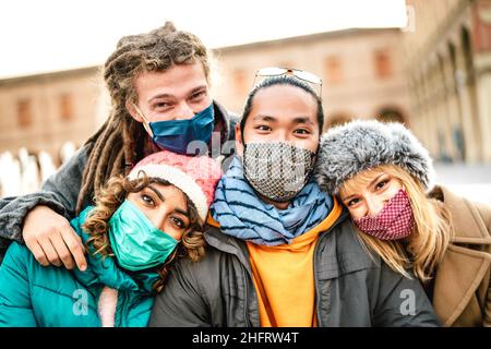 Multikulturelle Freunde, die Selfie machen, tragen Gesichtsmaske auf Winterkleidung - Neues Konzept des normalen Lebensstils mit jungen Menschen, die gemeinsam im Freien Spaß haben Stockfoto