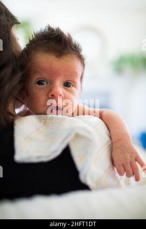 Kleiner Junge schaut mit großen Augen über die Schulter der Mutter. Stockfoto