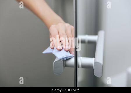 Reinigen Sie die Griffe der Glastür mit einem antiseptischen, feuchten Tuch. Desinfizieren Sie Oberflächen Prävention in Krankenhäusern und öffentlichen Räumen gegen Corona-Virus. Frauenhand Stockfoto