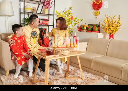 Glückliche Familie mit zwei Kindern, die zu Hause das chinesische Neujahr feiern und Tee, Obst und Süßigkeiten genießen Stockfoto