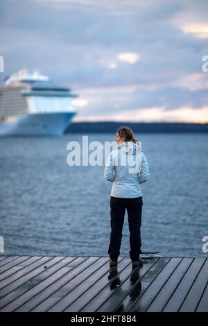 Frau steht auf dem Dock mit einem riesigen Kreuzschiff in der Ferne, Maine Stockfoto