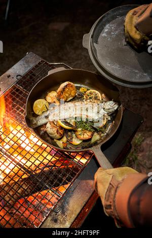 Der Koch kocht Forellen in einem Gusseisen über einem offenen Feuer. Stockfoto