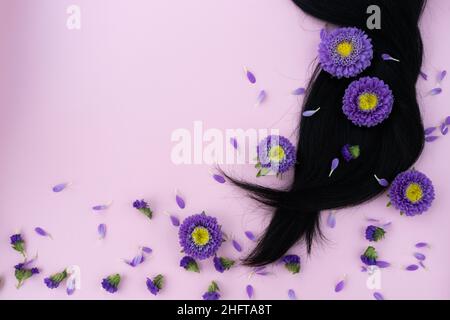 Schwarzes Haar mit Fliederblüten und Blütenblättern darauf. Haarpflegekonzept. Stockfoto