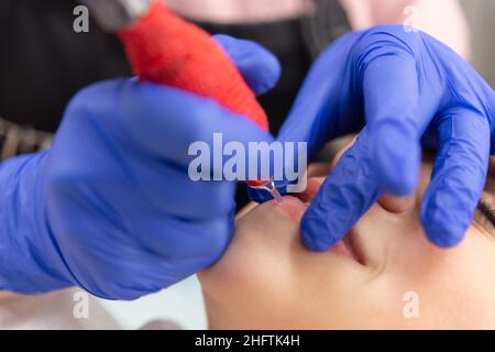 Junge Frau mit permanentem Make-up auf den Lippen im Kosmetiksalon. Lippentätowierung. Nahaufnahme. Stockfoto