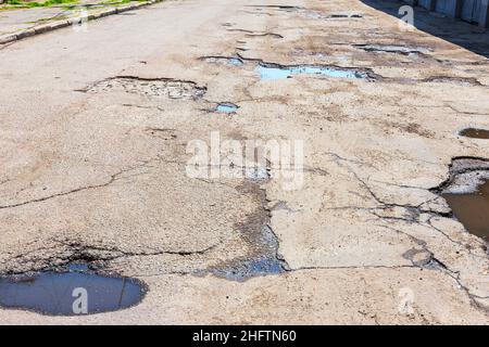 Eine durch Regen und Schnee beschädigte Straße, die gewartet werden muss. Zerbrochener Asphalt, der zu einem Schlagloch führt, das für Fahrzeuge gefährlich ist. Stockfoto