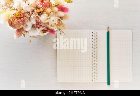 Offenes leeres Notizbuch mit türkisfarbenem Bleistift und schönem Bouquet von getrockneten Blumen Stockfoto