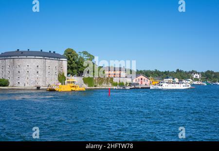 Gelbe Autofähre und weiße Passagierfähre fahren am Schloss Vaxholm im Stockholmer Archipel vorbei Stockfoto