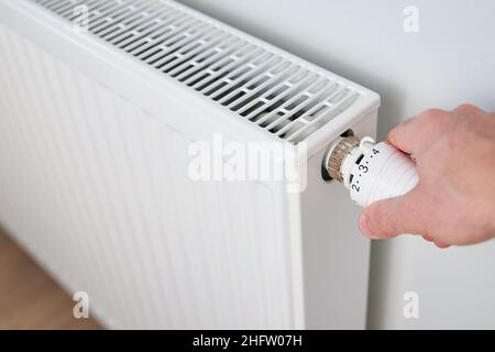 Die Temperatur am Heizkörper-Thermostat von Hand einstellen und den Heizkörper-Regler drehen, um die Wärme zu Hause zu steuern Stockfoto