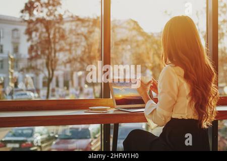 Nicht erkennbare Frau im Café, die auf das Fenster schaut, mit einem Laptop aus der Ferne arbeitet, Person, die während der Online-Arbeit eine Pause macht Stockfoto