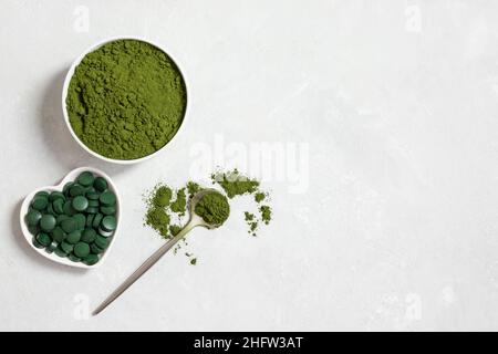 Grünes Chlorella-Pulver und Spirulina-Pillen auf weißem Betongrund. Natürliche mineralische Nahrungsergänzungsmittel für die Gesundheit. Blick von oben. Speicherplatz kopieren Stockfoto