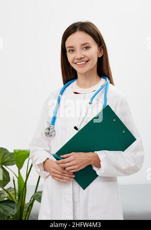 Arztberuf. Brünette Hausärztin mit Patientenakte in der Hand stehend in einer Klinik, Porträt Stockfoto
