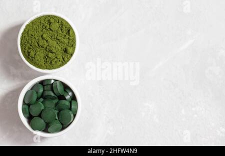 Chlorella und Spirulina in Schalen auf weißem Betongrund. Tabletten und Pulver bilden sich. Entgiften Sie Superfood. Gesunde Ergänzung. Platz kopieren, Draufsicht, f Stockfoto