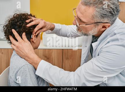 Audiologe, der ein Hörgerät auf das männliche Kinderohr legt, während er die Hörklinik besucht. Hörlösungen Stockfoto