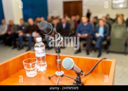 Modern ein akustisches Mikrofon auf dem Podium des Konferenzsaals auf dem defokussierenden Hintergrund eines vollgepackten Auditoriums im Saal, als Illustration Stockfoto