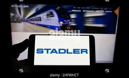 Person, die Smartphone mit Logo der Schweizer Stadler Rail AG auf dem Bildschirm vor der Website hält. Konzentrieren Sie sich auf die Telefonanzeige. Stockfoto