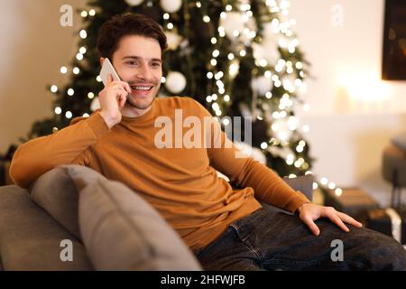 Ein fröhlicher Mann, der auf dem Handy spricht und auf der Couch sitzt Stockfoto