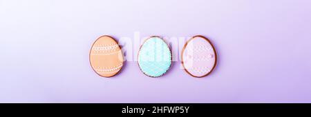 Frohe Ostern minimalistischer Hintergrund. Bunte Pastell ostereier Cookies auf einem violetten Hintergrund.Ostern Grußkarte mit bunten Lebkuchen.Mock up. Banner. Draufsicht. Stockfoto