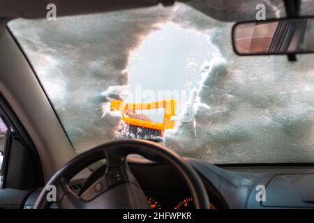 Mann, der die Windschutzscheibe mit Schaber und Bürste von Schnee und Eis reinigt Stockfoto