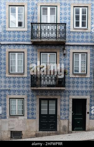 Architektonische Details Nahaufnahme der traditionellen blauen Fliesenfassade des Apartmentgebäudes mit gusseisernen Geländerbalkonen und Blumenkästen in Lissabon P Stockfoto