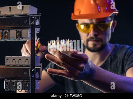 Ein Elektriker arbeitet in einer Schalttafel mit einem elektrischen Anschlusskabel. Stockfoto