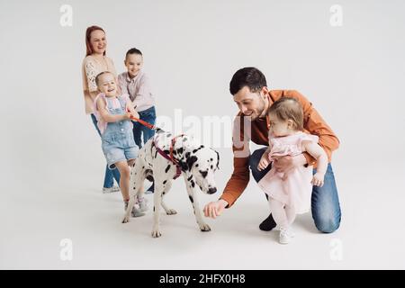 Junge Familie mit Kindern, die mit einem dalmatinischen Hund auf weißem Hintergrund spielen Stockfoto