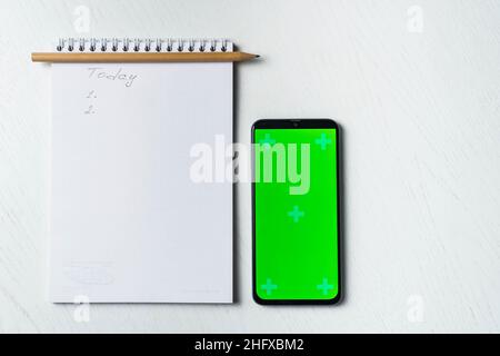 Weißer Notizblock mit Inschrift heute, Smartphone Green Screen Mockup und Bleistift flach legen. Tamplate für Design Stockfoto