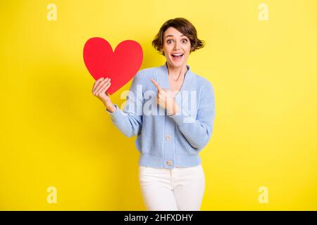 Portrait von attraktiven fröhlich erstaunt Mädchen demonstrieren Papier Herz amour isoliert über hellen gelben Hintergrund Stockfoto