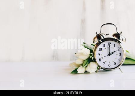 Konzept der Sommerzeit. Stellen Sie Ihre Uhren und auf 2 Uhr und Frühling voraus mit diesem Bild von einem Wecker mit weißen Tulpenblüten. Stockfoto