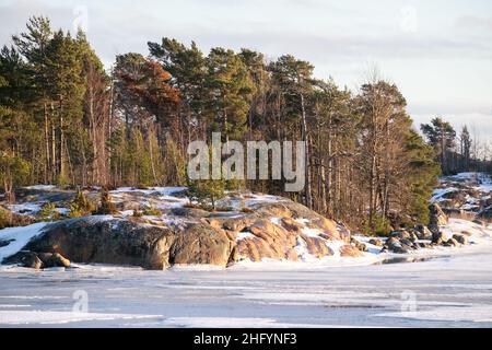 Helsinki / Finnland - 13. JANUAR 2022: Blick auf eine kleine Insel über einen gefrorenen Fluss an einem sonnigen Wintertag. Stockfoto