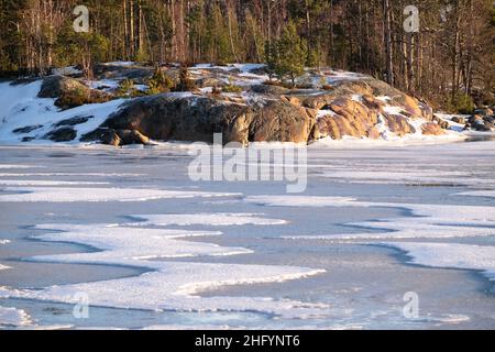 Helsinki / Finnland - 13. JANUAR 2022: Blick auf eine kleine Insel über einen gefrorenen Fluss an einem sonnigen Wintertag. Stockfoto