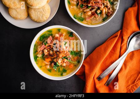 Schinken-Knochen-Suppe mit weißen Bohnen und Grünkohl serviert mit Buttermilchkeksen: Schalen mit Hambone-Suppe mit Cannellini-Bohnen und Baby-Grünkohl serviert mit Keks Stockfoto