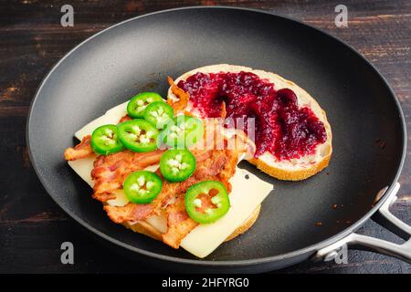 Braten eines Blackberry Bacon Gegrilltes Käse-Sandwich in einer Pfanne: Zwei Hälften eines gegrillten Käse-Sandwiches mit Speck in einer beschichteten Pfanne Stockfoto