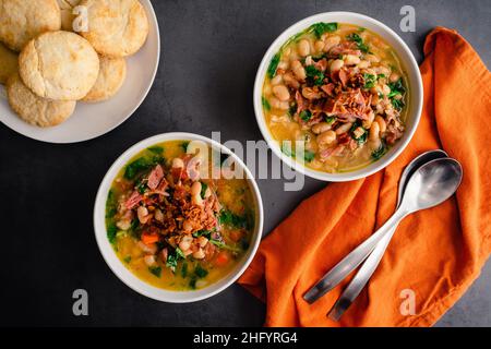 Schinken-Knochen-Suppe mit weißen Bohnen und Grünkohl serviert mit Buttermilchkeksen: Schalen mit Hambone-Suppe mit Cannellini-Bohnen und Baby-Grünkohl serviert mit Keks Stockfoto